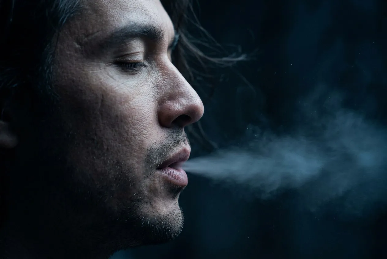側臉極近特寫，閉眼微張口緩緩吐氣，呼吸化為銀藍色光霧溶入黑暗空氣中