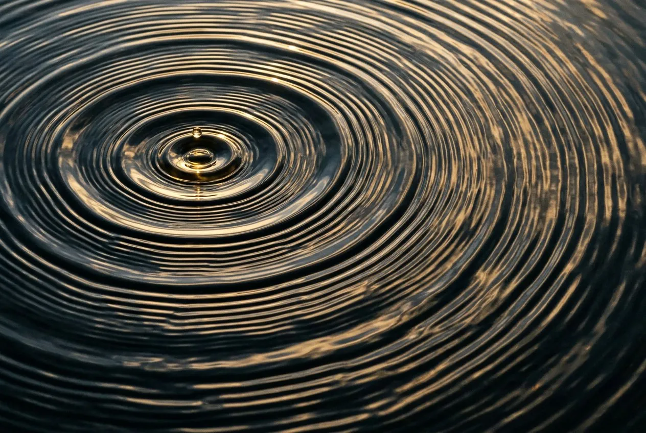 俯拍水面漣漪從單一水滴衝擊點向外擴散，同心圓充滿整個畫面，傍晚斜光在水面形成明亮高光與暗色波谷，衝擊點位於左上三分之一處